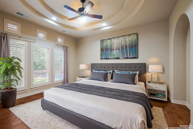 bedroom with recessed lighting, baseboards, wood finished floors, a tray ceiling, and visible vents
