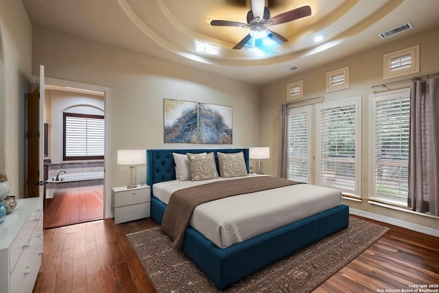 bedroom with dark wood-style flooring, a tray ceiling, and visible vents