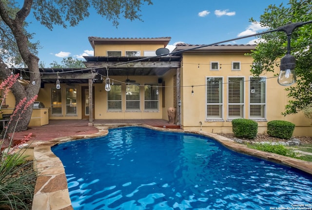 rear view of property with a patio, a ceiling fan, an outdoor pool, and stucco siding