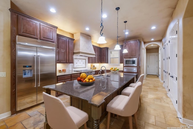 kitchen featuring built in appliances, stone tile floors, recessed lighting, custom range hood, and a warming drawer