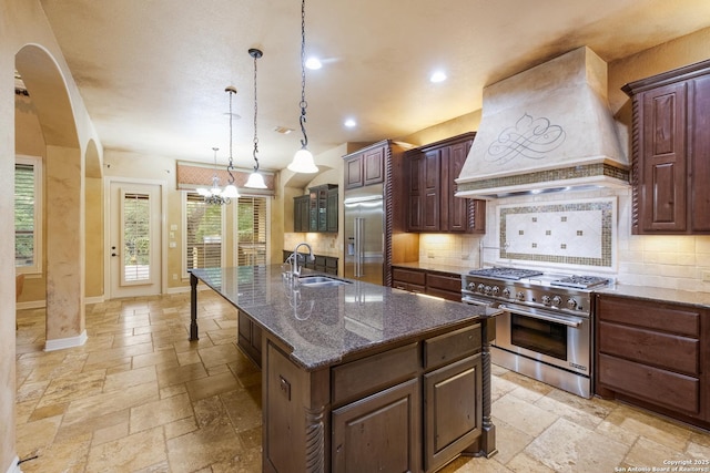 kitchen with stone tile floors, high end appliances, custom exhaust hood, a sink, and backsplash