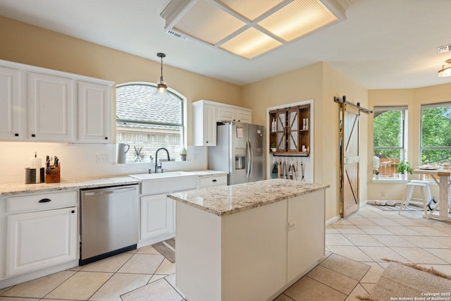 kitchen with a barn door, white cabinets, a sink, light tile patterned floors, and stainless steel appliances