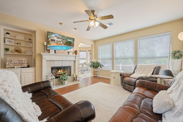 living area featuring visible vents, wood finished floors, a fireplace, built in shelves, and a ceiling fan