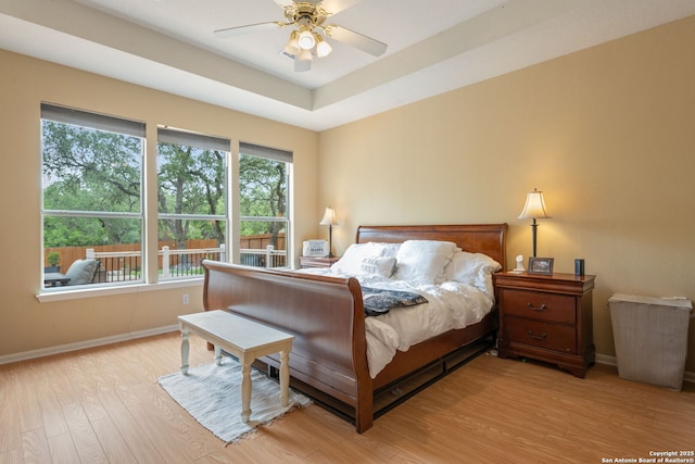 bedroom featuring baseboards, ceiling fan, a raised ceiling, and light wood-style floors