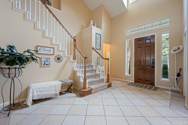 foyer entrance with baseboards, a towering ceiling, light tile patterned flooring, and stairway