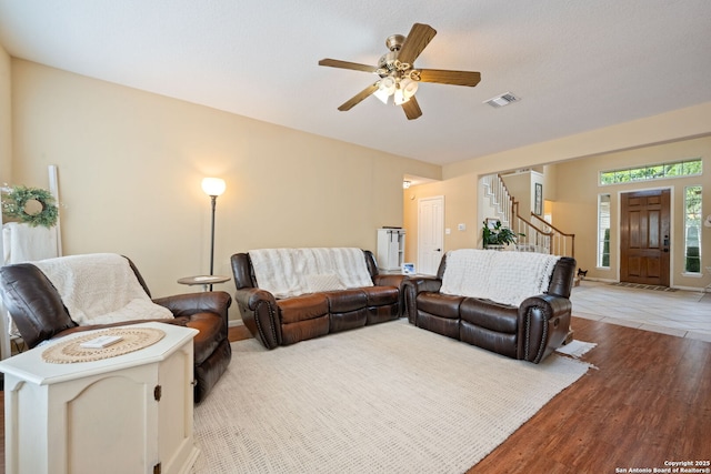 living area with visible vents, a ceiling fan, light wood finished floors, and stairway