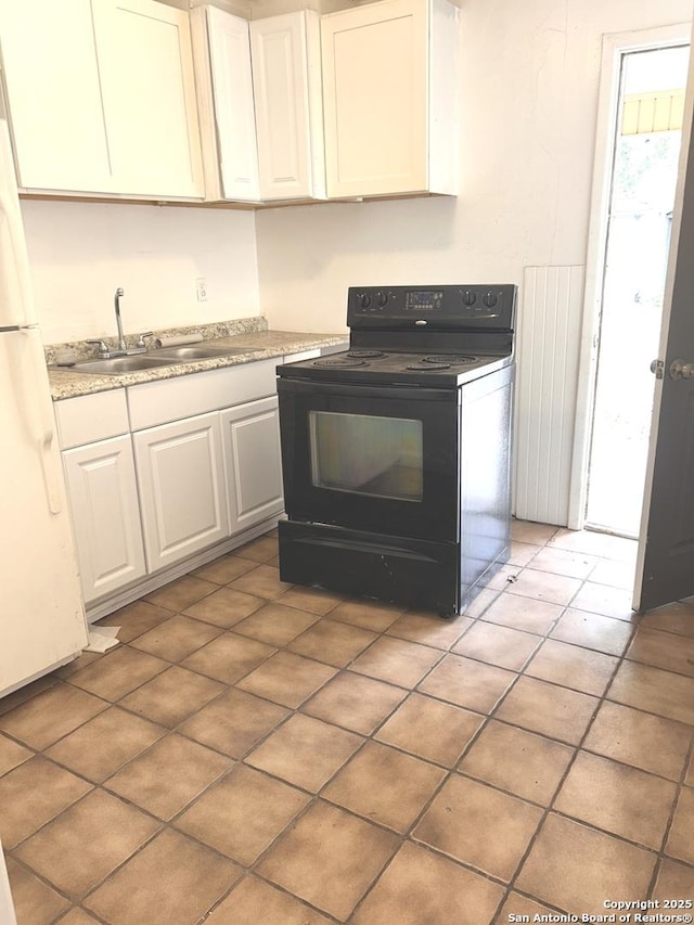 kitchen with black electric range oven, a sink, light countertops, white cabinets, and freestanding refrigerator