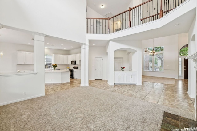 unfurnished living room featuring decorative columns, light colored carpet, an inviting chandelier, a high ceiling, and light tile patterned flooring