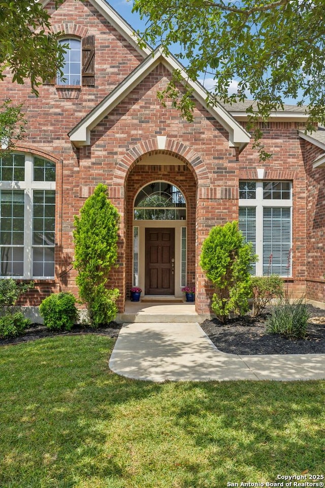 view of exterior entry featuring brick siding and a yard