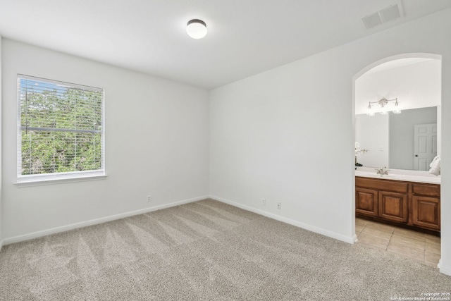 unfurnished bedroom with light colored carpet, a sink, arched walkways, baseboards, and visible vents