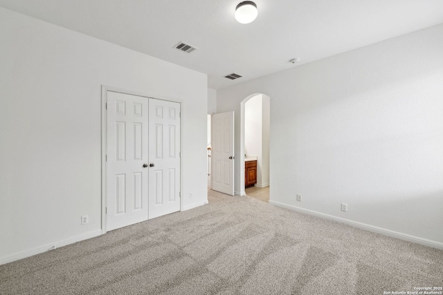 unfurnished bedroom with light colored carpet, arched walkways, baseboards, and visible vents