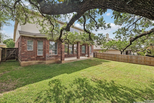 rear view of property with brick siding, a patio, a fenced backyard, and a lawn