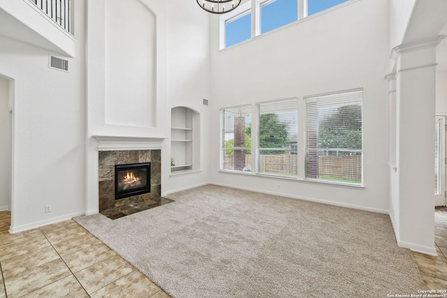 unfurnished living room featuring built in features, a towering ceiling, baseboards, a tile fireplace, and carpet