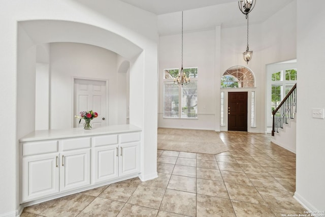 foyer entrance featuring an inviting chandelier, light tile patterned flooring, baseboards, stairway, and arched walkways