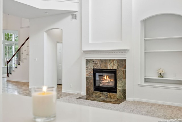unfurnished living room featuring built in features, stairs, baseboards, a tile fireplace, and visible vents