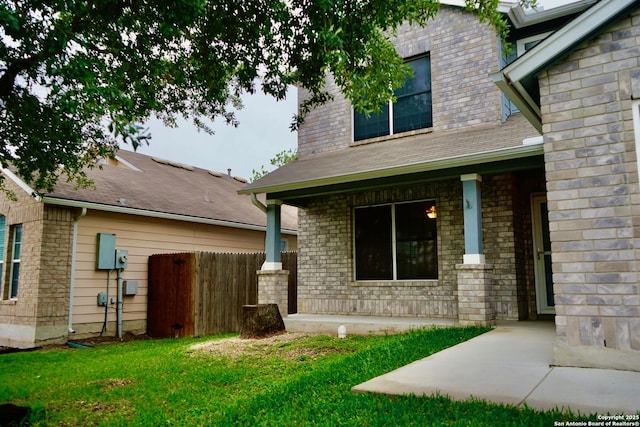 doorway to property featuring fence, a shingled roof, a yard, and a porch