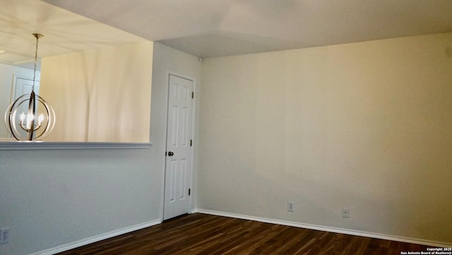 spare room with dark wood-type flooring, baseboards, and a chandelier