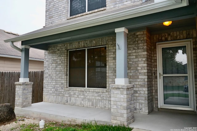property entrance with fence, covered porch, and brick siding