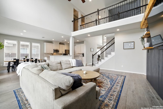 living area with stairway, a high ceiling, light wood-type flooring, and ceiling fan