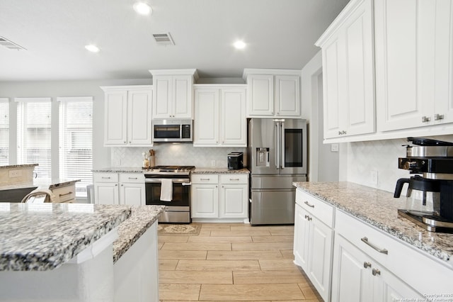 kitchen with appliances with stainless steel finishes, tasteful backsplash, white cabinets, and visible vents