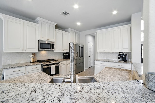kitchen with backsplash, visible vents, appliances with stainless steel finishes, light stone countertops, and white cabinetry