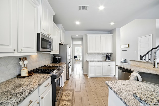 kitchen featuring visible vents, light wood-type flooring, white cabinets, tasteful backsplash, and appliances with stainless steel finishes