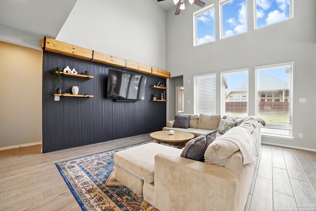 living room featuring a ceiling fan, high vaulted ceiling, baseboards, and light wood-type flooring