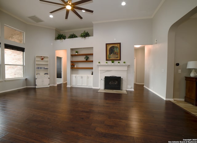unfurnished living room featuring ceiling fan, crown molding, arched walkways, a fireplace with flush hearth, and wood-type flooring