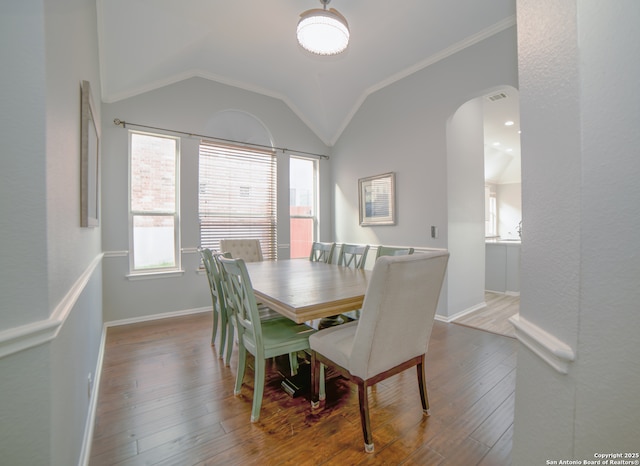 dining area with crown molding, wood-type flooring, arched walkways, baseboards, and vaulted ceiling