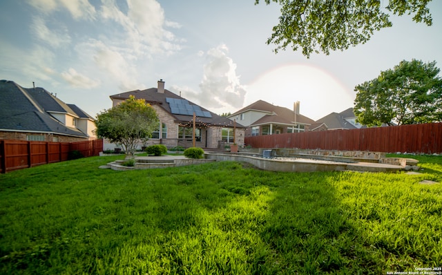rear view of house featuring a fenced backyard, a chimney, a yard, and roof mounted solar panels