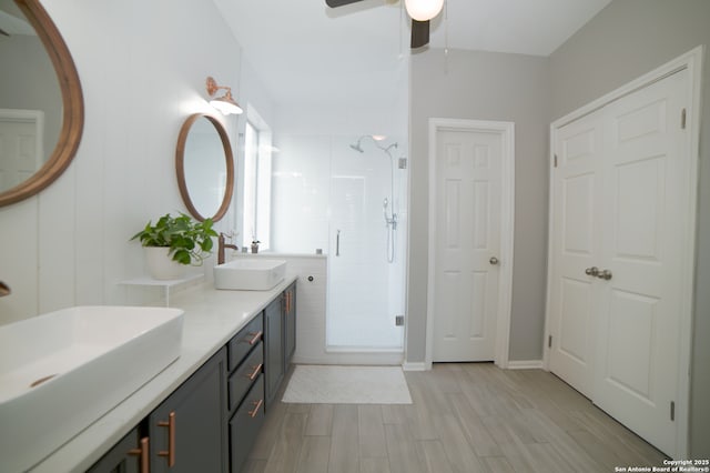 bathroom featuring double vanity, a shower stall, a sink, and wood finished floors