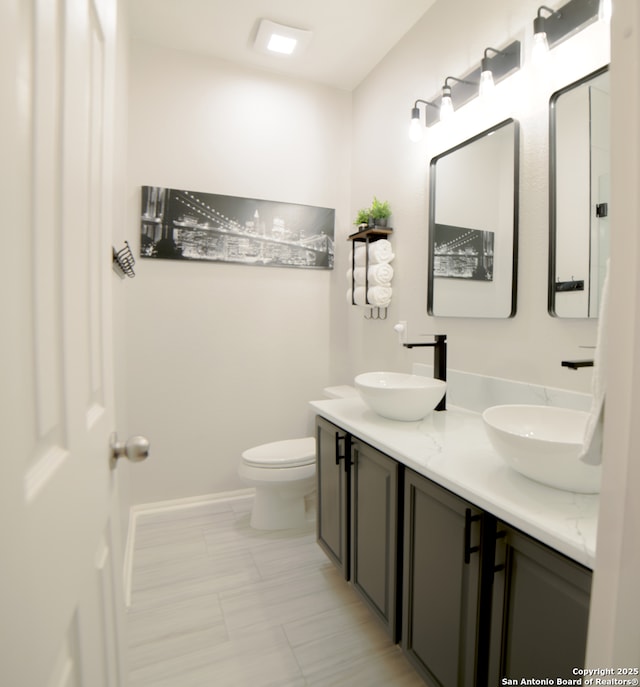 bathroom with a sink, baseboards, toilet, and double vanity