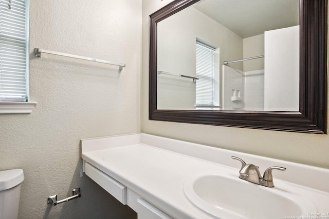 bathroom with toilet, a textured wall, a shower, and vanity