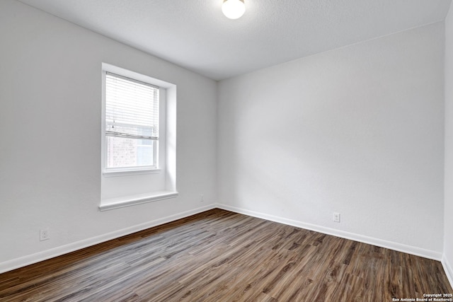 spare room featuring baseboards and dark wood-type flooring