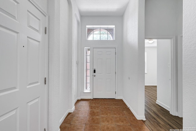 entrance foyer featuring dark tile patterned floors, a textured wall, and baseboards