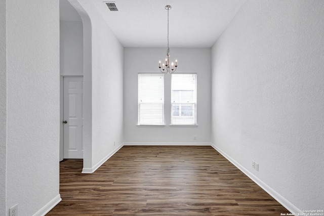 unfurnished dining area featuring visible vents, a textured wall, arched walkways, dark wood finished floors, and a notable chandelier