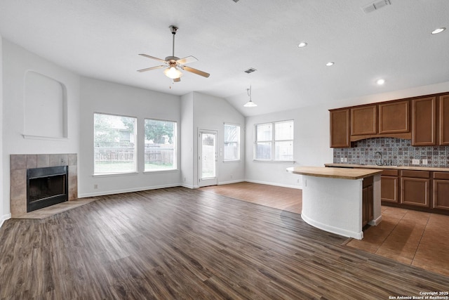 kitchen with lofted ceiling, baseboards, open floor plan, a tiled fireplace, and a ceiling fan