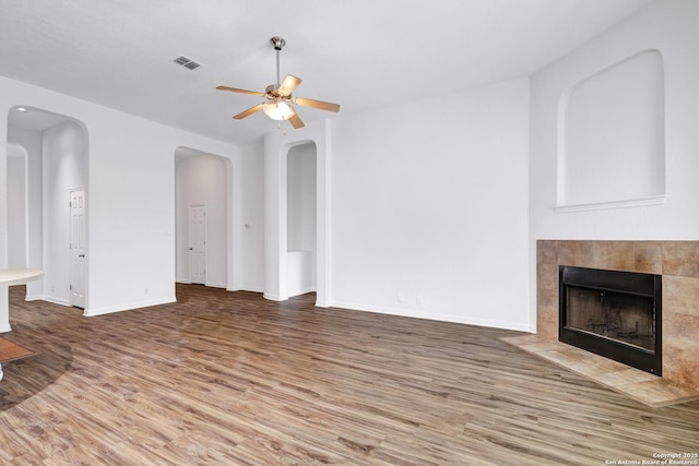 unfurnished living room with a ceiling fan, visible vents, a fireplace, wood finished floors, and baseboards