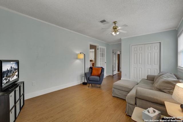 living room with light wood finished floors, a textured ceiling, a ceiling fan, visible vents, and ornamental molding