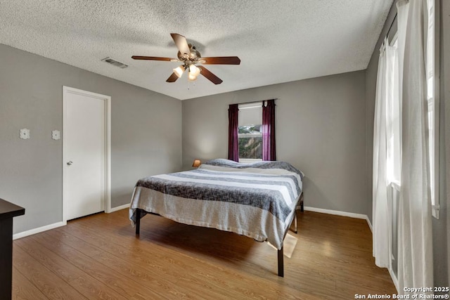 bedroom featuring baseboards, a textured ceiling, visible vents, and wood finished floors