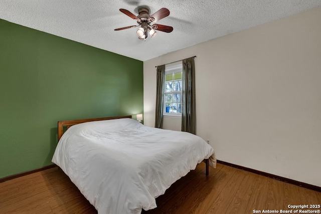 bedroom with a textured ceiling, baseboards, a ceiling fan, and wood finished floors