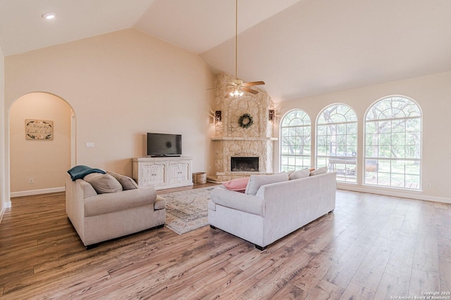 living area with wood finished floors, baseboards, ceiling fan, high vaulted ceiling, and arched walkways