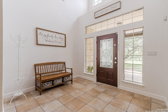 foyer entrance with light tile patterned flooring, baseboards, and a high ceiling