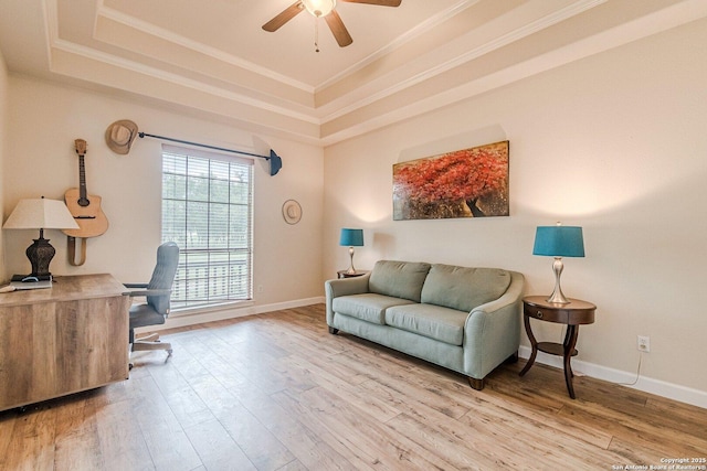 living area featuring ceiling fan, crown molding, wood finished floors, baseboards, and a tray ceiling