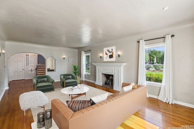 living room featuring baseboards, arched walkways, wood finished floors, and a fireplace