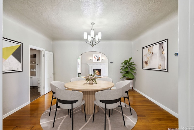dining area featuring an inviting chandelier, wood finished floors, baseboards, a textured ceiling, and arched walkways