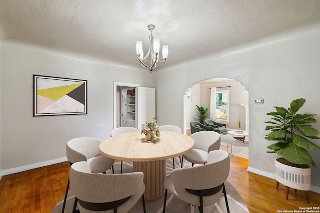 dining room with arched walkways, a textured ceiling, wood finished floors, and a notable chandelier