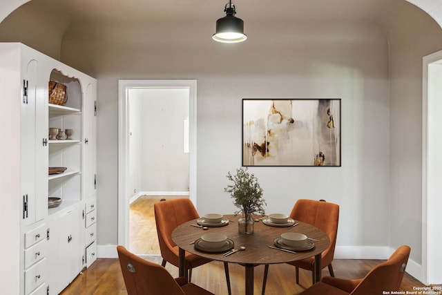 dining room with arched walkways, baseboards, and wood finished floors