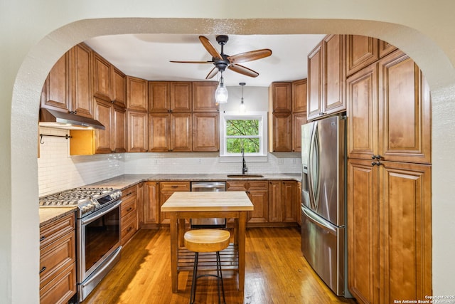 kitchen featuring brown cabinets, ceiling fan, a sink, stainless steel appliances, and under cabinet range hood