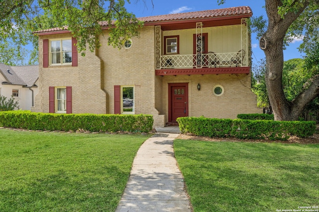 mediterranean / spanish house featuring brick siding, a balcony, and a front lawn